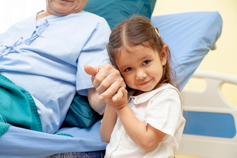 Grandparent in a hospital bed holding hands with grandchild