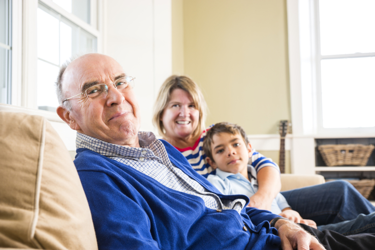 Happy senior citizen sitting on the couch with his daughter and grandson